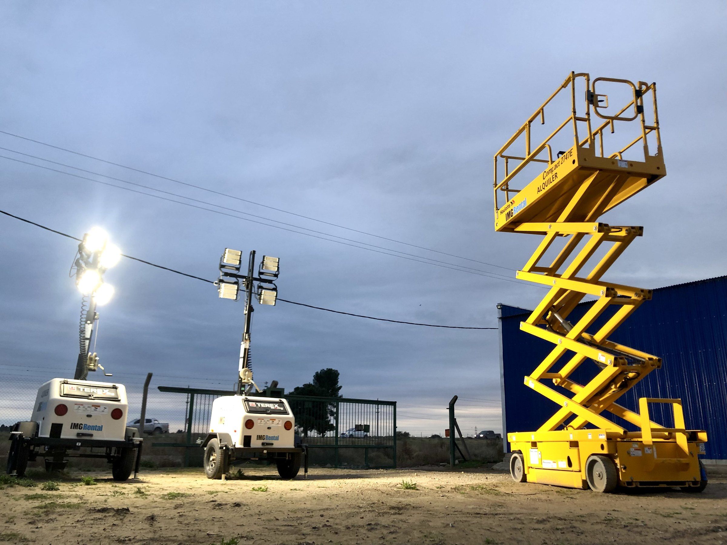 Plataforma tijera y torres de iluminación trabajando al atardecer