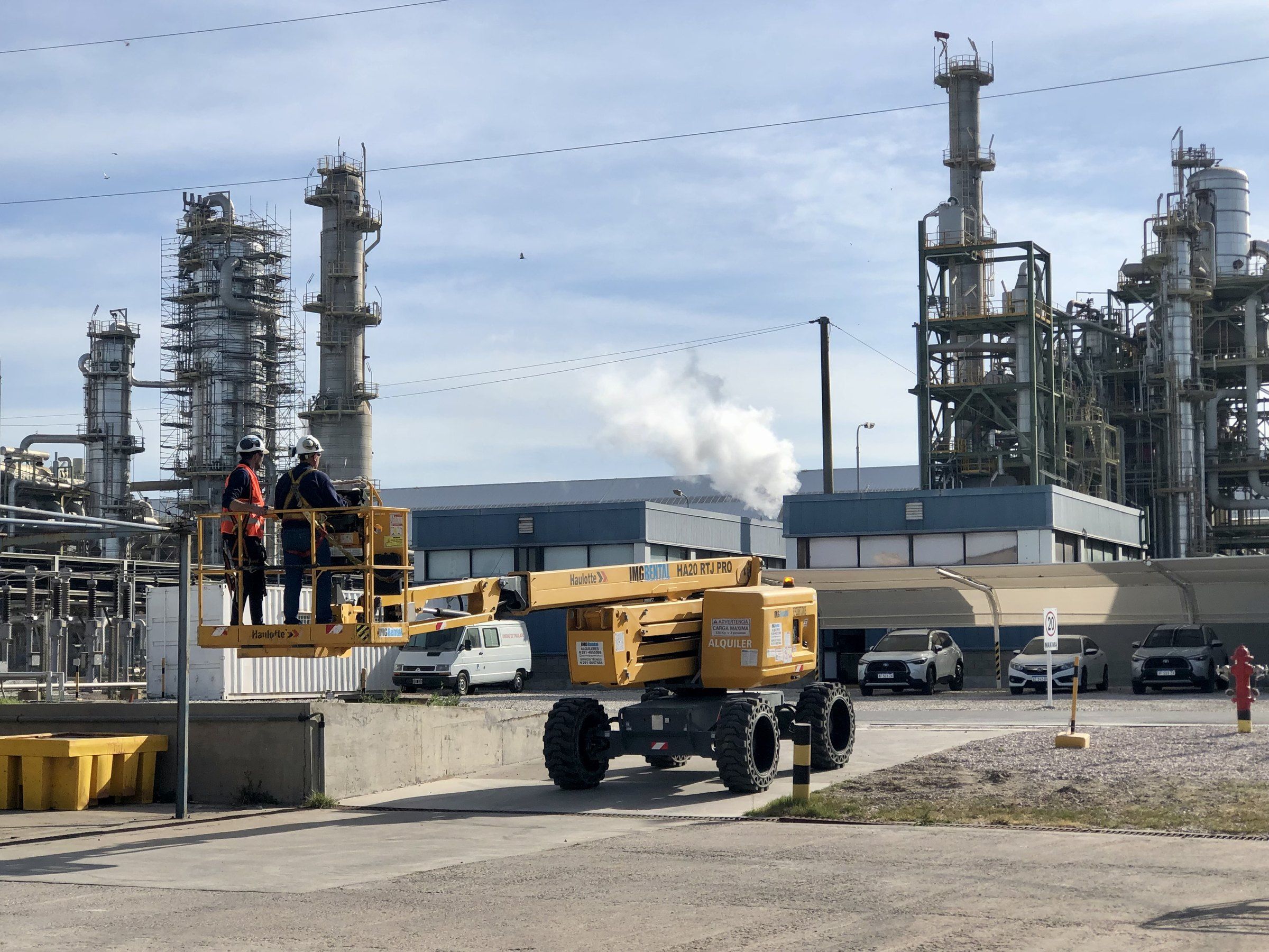 Brazo articulado con operarios con equipo de protección frente a una refinería