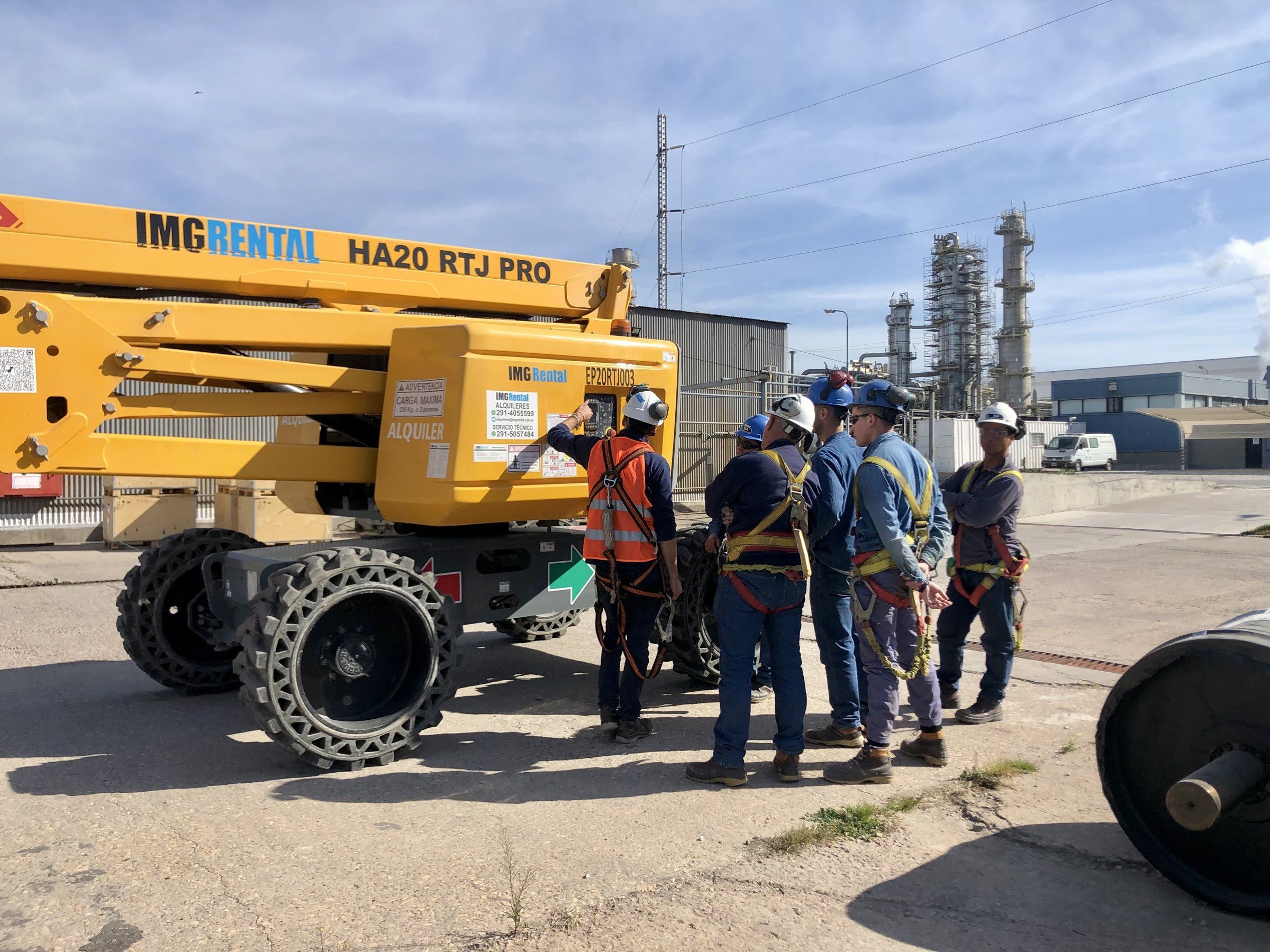 Técnicos y operarios con arnés y casco revisando un brazo articulado antes de trabajar